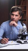 A man in a shirt and tie sitting at a desk with a microscope video