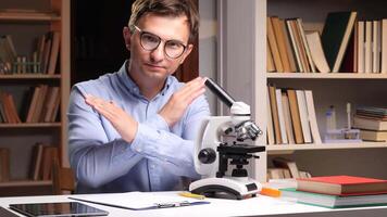 A man in glasses is sitting at a desk with a microscope video