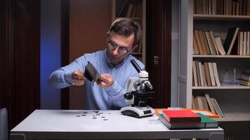 A man in glasses is looking at coins in a microscope video