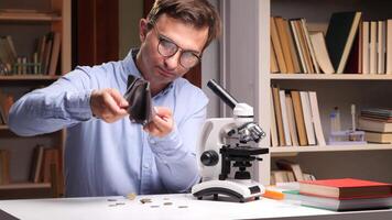 A man in glasses holding a coin in front of a microscope video