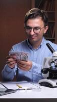 A man in glasses is holding money in front of a microscope video