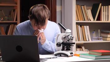 A man in a lab coat is blowing his nose while looking at a microscope video