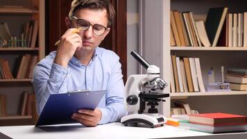 A man in glasses is looking at a clipboard with a microscope video