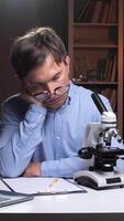 A man with glasses and a microscope in front of a laptop video