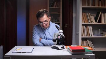 A man in glasses sits at a desk with a microscope video
