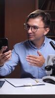A man in glasses is using his phone while looking at a microscope video