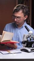 A man in glasses is looking at a book and a microscope video