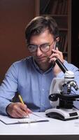 A man in glasses talking on the phone while looking at a microscope video