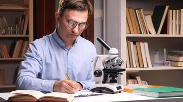 A man in glasses is writing on a book with a microscope video