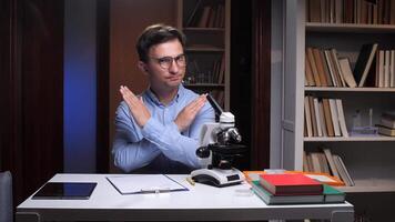 A man in glasses sitting at a desk with a microscope video