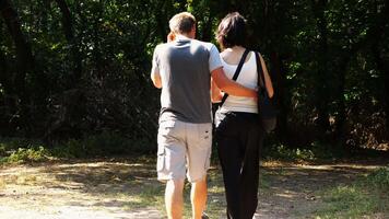 Happy couple walking along path at summer forest. Romanti pair going along trail at wild woodland. Lovers spending time together at nature. Concept of love and happiness. Slow motion video