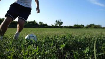 Male feet professional footballer shows tricks with ball while running at green field. Legs of sportsman kicks ball during jogging at meadow on sunny day. Young man training at stadium. Slow motion video