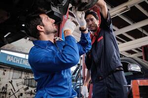 Two male mechanics, Hispanic and Asian workers fixing automotive wheels and maintaining car suspensions in garage station, and technician engineering service jobs in vehicle transport industry. photo