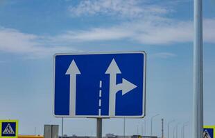 Traffic sign displays arrows showing the option to continue straight or turn right at an intersection in sunny weather photo