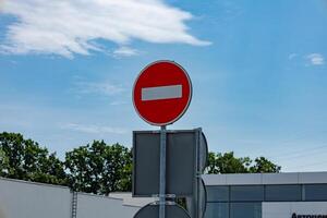 A circular no entry sign stands prominently against a blue sky, indicating restricted access to vehicles near a contemporary structure photo