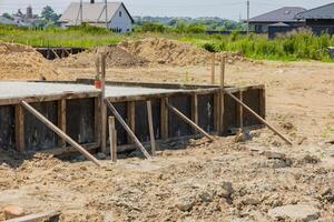 Workers are setting up a foundation with wooden supports at a construction site surrounded by greenery and houses photo