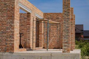 New brick house construction reveals unfinished walls and scaffolding, highlighting ongoing building activities in a residential neighborhood photo