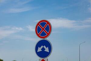 Road signs indicate no parking regulations and a yield instruction against a clear blue sky in an urban environment photo