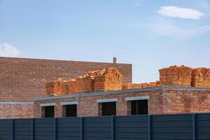 Bricks are neatly stacked on a building structure at a construction site, surrounded by a blue sky. The setting reflects a sunny summer day photo