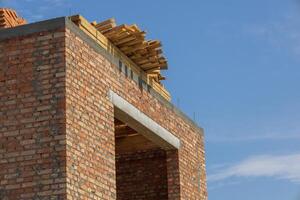 A brick structure is being built with wooden beams resting on top, showcasing ongoing construction against a bright sky photo