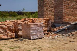 Bright sunlight illuminates a construction site featuring neatly stacked bricks beside a partially built structure, indicating ongoing development photo