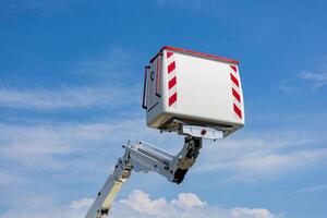 Work platform raised high against a blue sky with clouds, ready for maintenance tasks in an outdoor environment during daylight photo