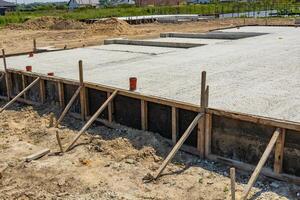 Workers are establishing a concrete foundation at a construction site surrounded by natural landscape during clear weather photo