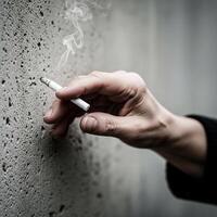 hand holding a burning cigarette with smoke against a concrete wall photo