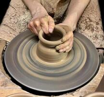 Hobbies and creativity. Closeup of clay product being made on pottery wheel. Hands of young craftsman forming clay pot on pottery wheel. photo