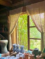 Window in country house with curtains made of coarse burlap, clay products on windowsill. Potters workshop. photo