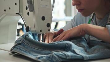 Person is working on jeans repair using industrial sewing machine. Focus is on hands and denim as material moves through machine. video