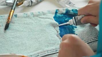 A close-up shot of a child customizing their clothes by applying paint to their jeans and creating a unique design. High angle. video
