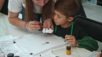 Drawing teacher helps young boy learn how to color T-shirts and other clothes in order to create unique designs and develop his creativity. video