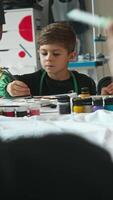 Teenage boy enthusiastically participates in drawing during art lessons at school. He dips a paintbrush into a palette and begins to draw. High angle. video