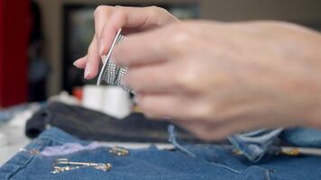 A craft clothing designer uses rhinestone trim spools to create a unique design for jeans. Close up. video