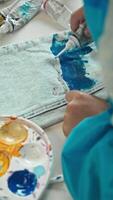 The artist uses paint from a tube to create a unique design on the leg of his jeans, resulting in a one-of-a-kind craft. Vertical. High angle. video