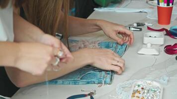 Skilled craftswoman in denim gives old jeans new and fashionable look by decorating them with various decorative elements in her workshop. video