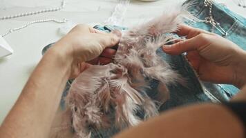 A fashion creator transforms vintage jeans by incorporating unique elements, such as ornamental feathers, into their design. video