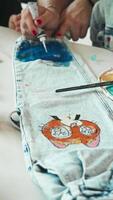 Mother assists her child in the process of transforming old jeans into unique creations by applying decorative touches with paints. Vertical. video
