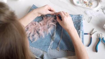In her workshop, dressmaker creates unique pieces of clothing from old shorts. She carefully decorates and complements them, creating unique look. High angle. video