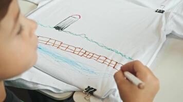The boy demonstrates his creativity by creating a T-shirt with a marker and drawing on it. High angle. Close up. video