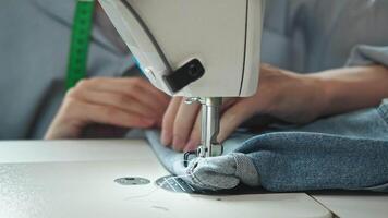Close-up shot of the working parts of a white sewing machine, as used by a seamstress, while she is embroidering a seam onto a denim fabric. video