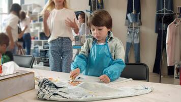 A loving mother is observing her child as they work on drawing project at workshop where they learn how to create clothing using their own designs. video