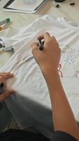 A teenager starts to draw on a white T-shirt using a black marker, creating a unique clothing design by hand. video
