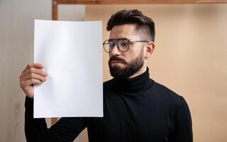 A man with glasses holding up a blank sheet of paper photo