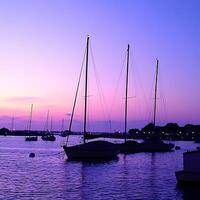 Serene Sunset Harbor Sailboats at Dusk. Silhouetted sailboats peacefully rest in a harbor as the sun sets, casting a vibrant purple glow on the water. photo