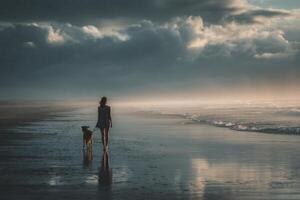 A woman and her dog walk along the beach at sunset photo