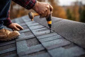 A man is using a nail gun to install a roof shingle photo