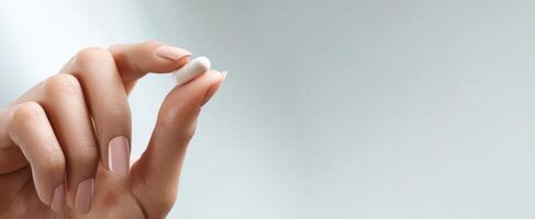 The hand holding a white pill against a soft background. photo