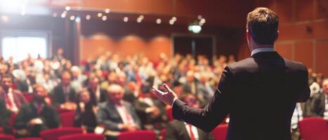 The speaker engaging a large audience during a corporate conference event. photo